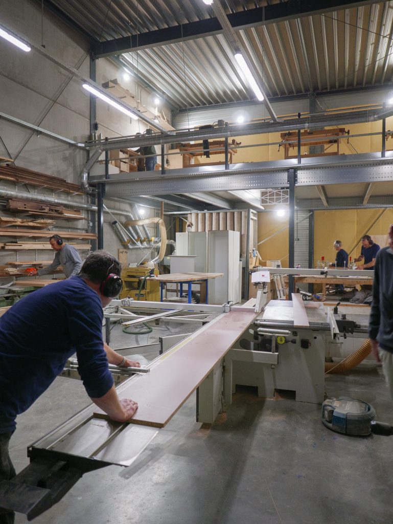 Studenten volgen een cursus meubelmaken en houtbewerking in een moderne werkplaats met diverse machines en gereedschappen.